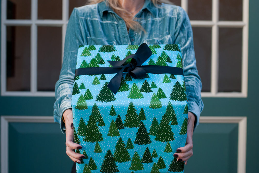 woman holding a box wrapped with christmas tree printed wrappers