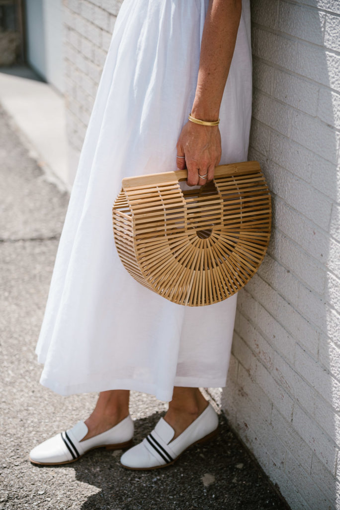 woman wearing one of the white summer dresses, white shoes, and holding a handbag