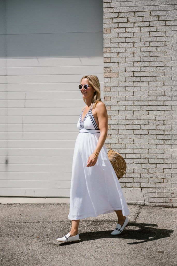 woman walking and wearing white dress, white flats, and a bag