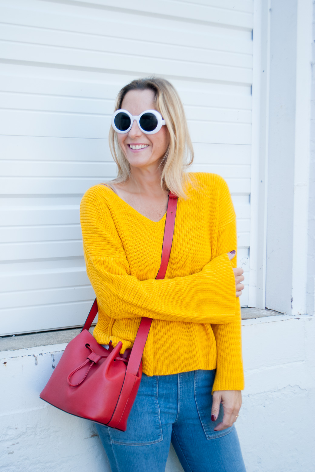 a woman wearing marigold fall color sweater and white sunnies and jeans