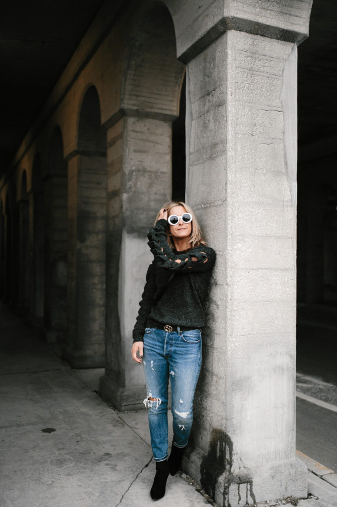 woman leaning on a wall and wearing go sweater night and jeans 