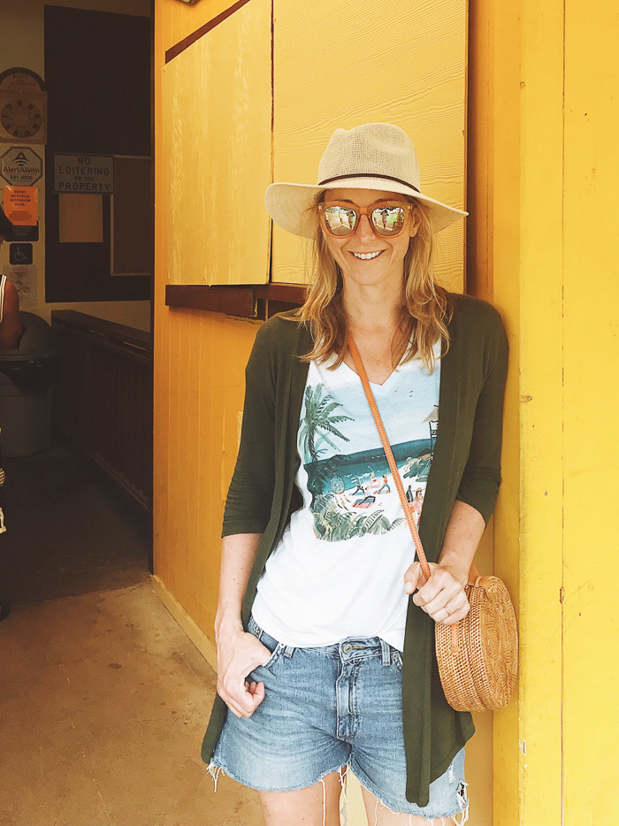 woman wearing Denim Shorts, White Graphic Tee, Panama Hat, Straw Purse, Moss Green Cardigan