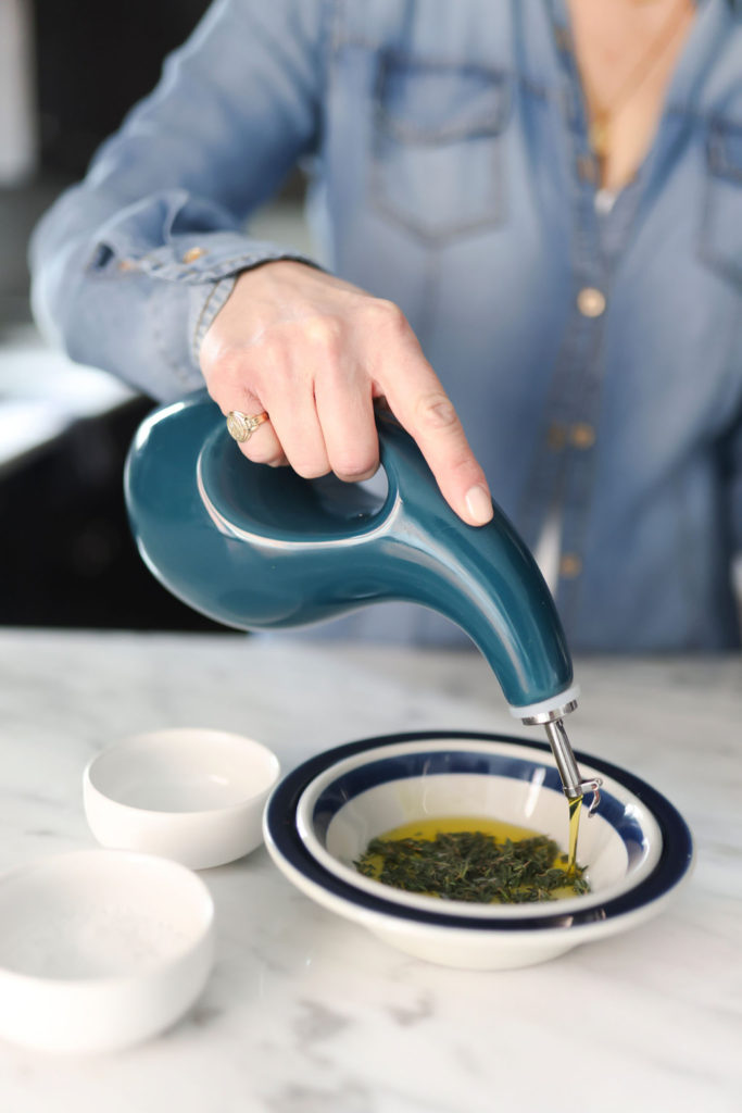 person adding olive oil in a bowl with herbs